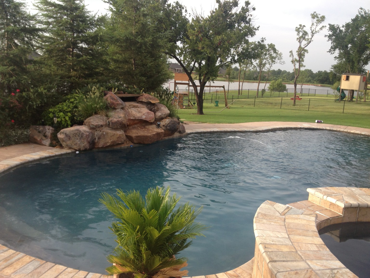 Another view of a completed freeform pool, rock feature, and stone-clad spa