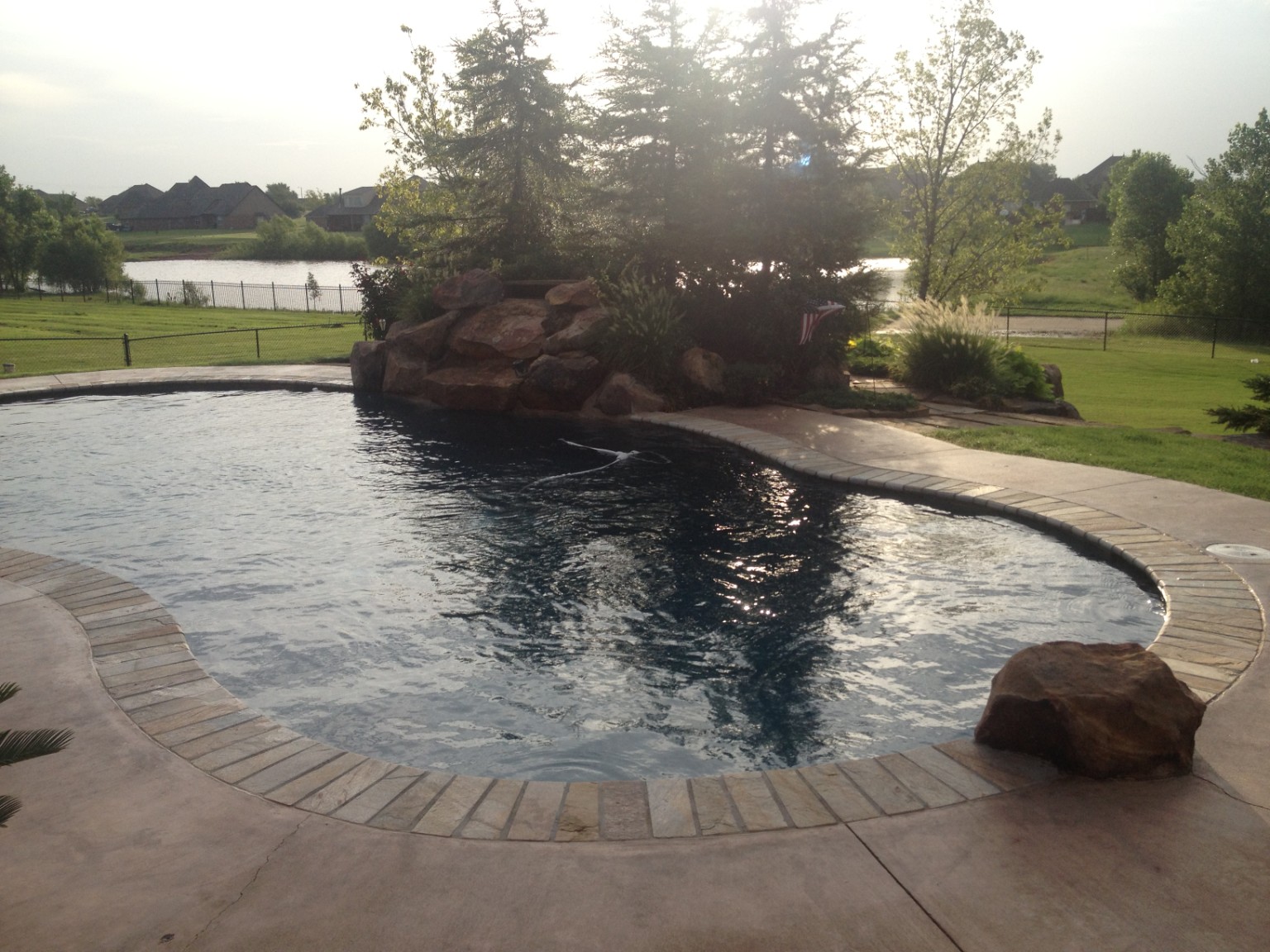 Completed freeform swimming pool with natural boulder feature and curved stone coping